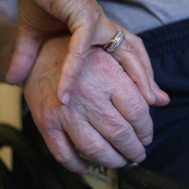 A nursing home resident holds his wife’s hand.